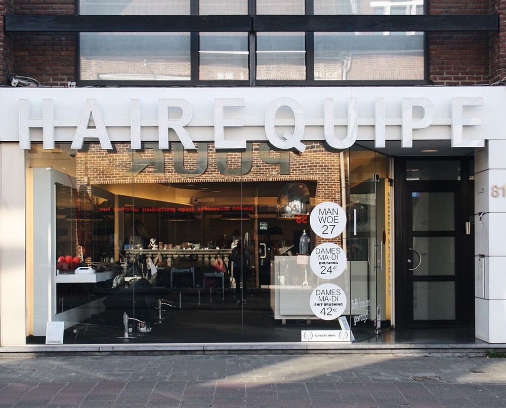 Voorzijde van een kapsalon met het opschrift "HAIREQUIPE", en prijsaankondigingen voor diensten.