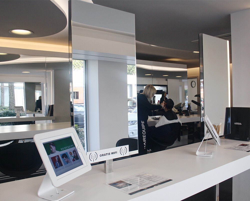 Interieur van een kapsalon met een styliste die een klant knipt, een tablet met informatie en een bordje voor gratis wifi.