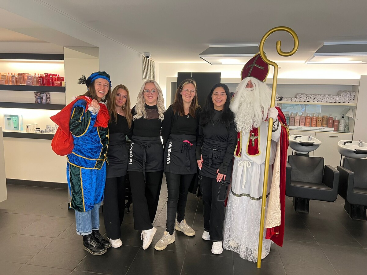 Groep van zes mensen poseert in een salon, met een persoon verkleed als Sinterklaas en een ander als Zwarte Piet.