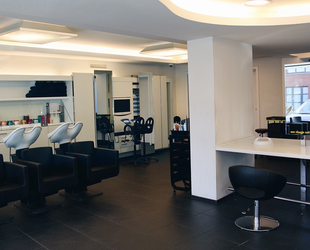 Interieur van een kapsalon met zwarte stoelen, wastafels, kasten en grote spiegels.