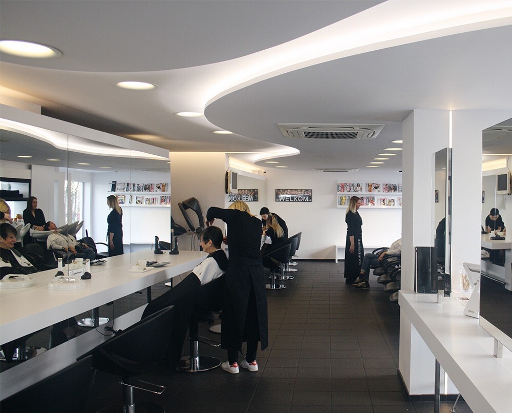 Een moderne kapsalon met meerdere stoelen, spiegels en klanten die worden bediend door kappers in zwarte kleding.
