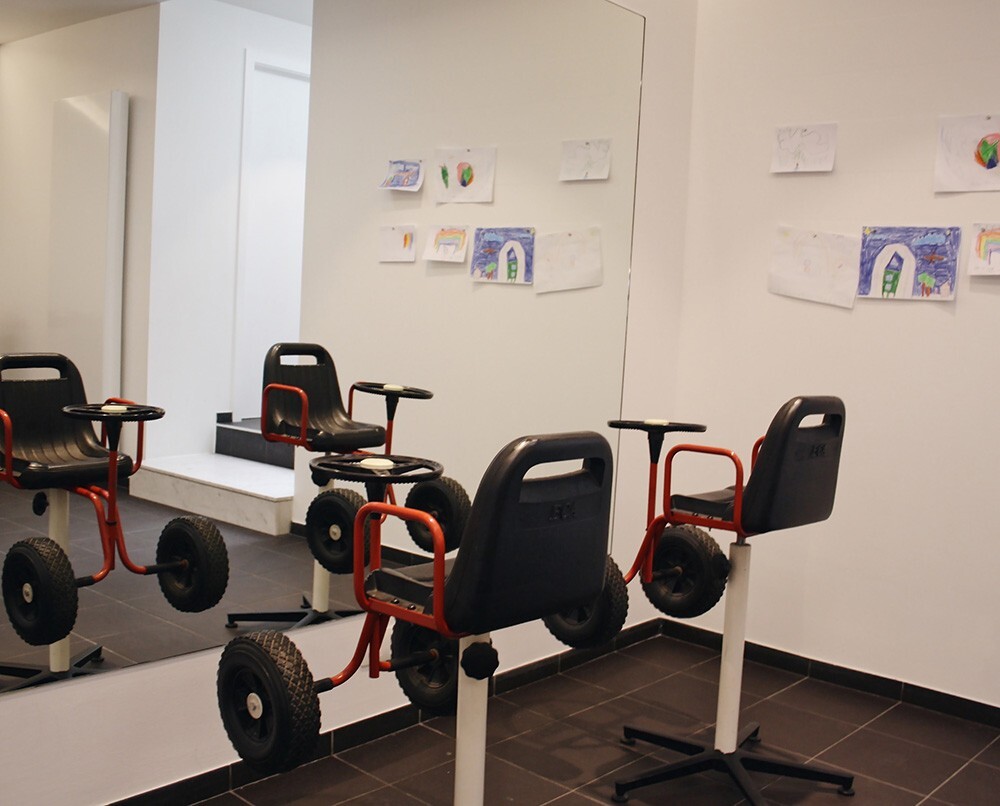 Een speelse ruimte met drie kinderfietsen voor een spiegel, omringd door getekende kunstwerken aan de muur.